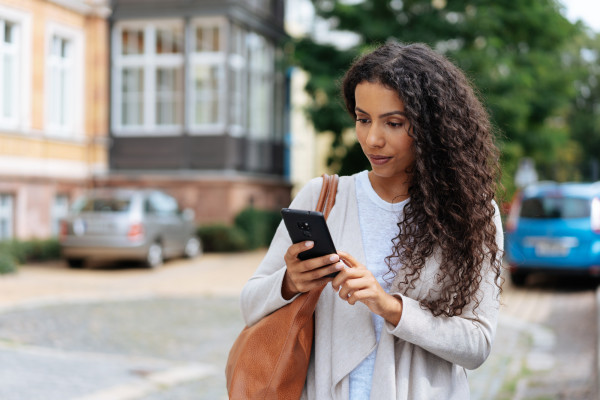 Woman with curly hair outside looking at her phone