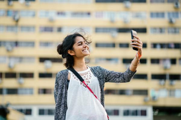 A smiling young South East Asian woman takes a selfie with her phone