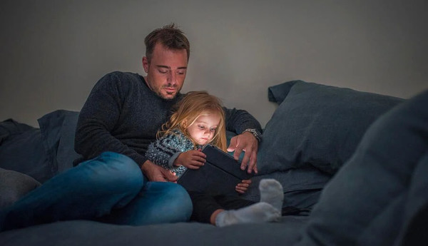 A father and daughter using a tablet while sitting on the couch.