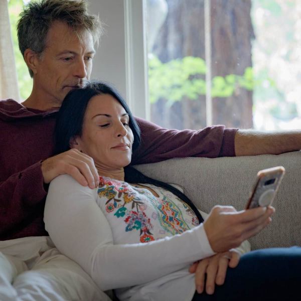A white middle-aged couple snuggle on the couch and look at the woman's phone