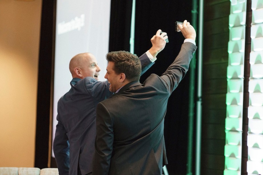 Scott sanders and Michael DeSouza take selfies on the partner summit stage