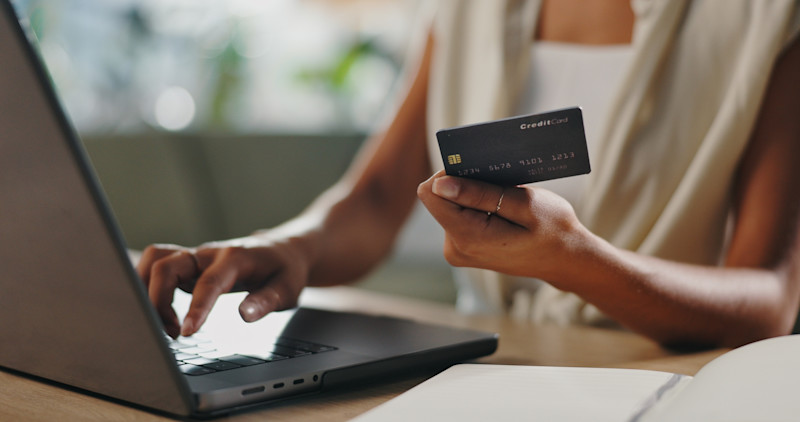 Zoom in of a woman holding a credit card while typing on her laptop