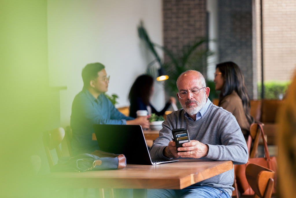 Man checking phone while sitting in front of laptop at a cafe