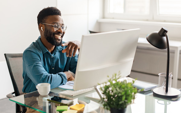 A black man works at a computer desk while smiling. 