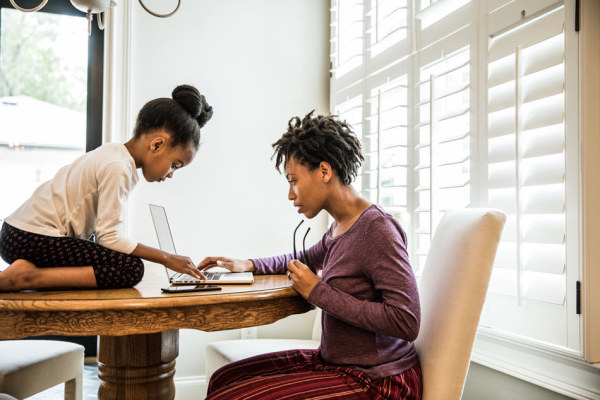 Mom and daughter at kitchen table, using a laptop.  Daughter on table.