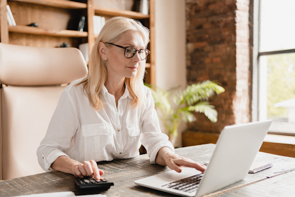 Older woman with glasses sitting at a desk and looking at her laptop