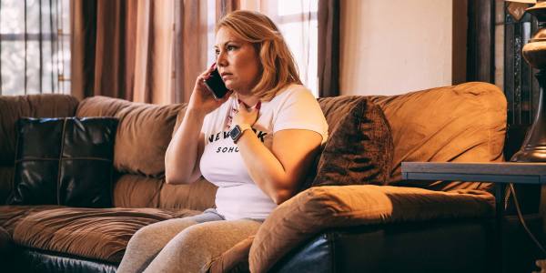 Concerned looking woman speaking on the phone while sitting on the couch. JPG