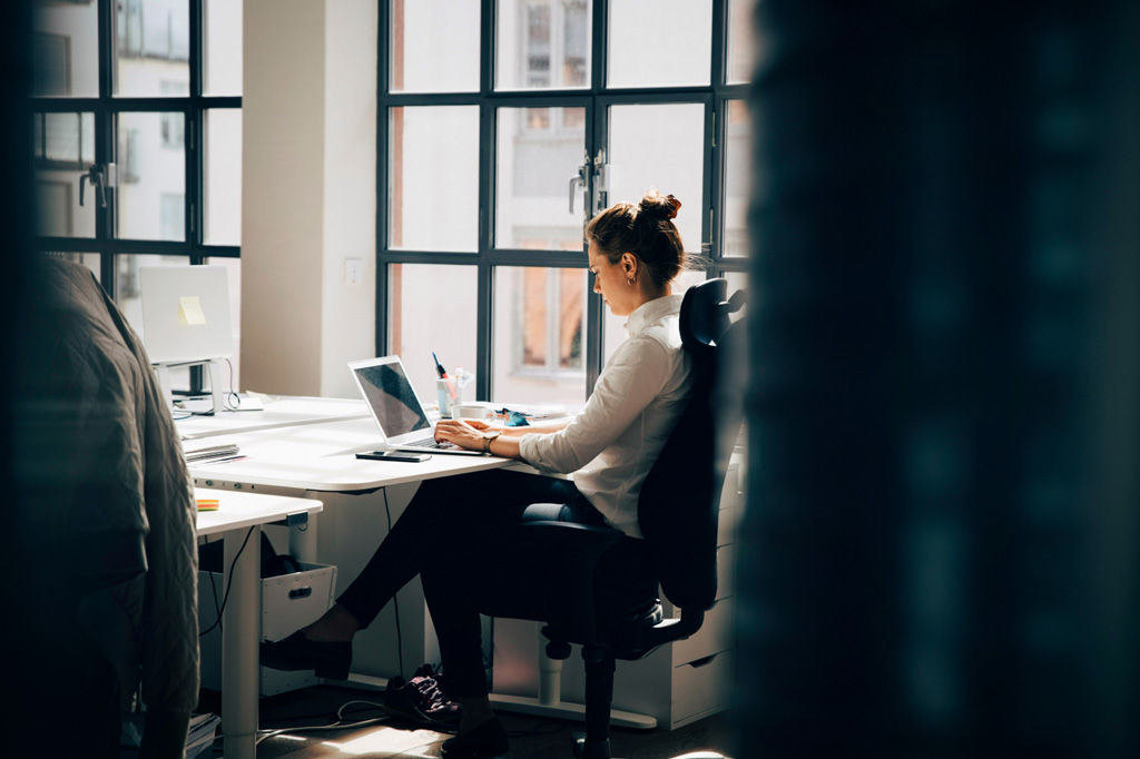 A woman working at her laptop by windows.