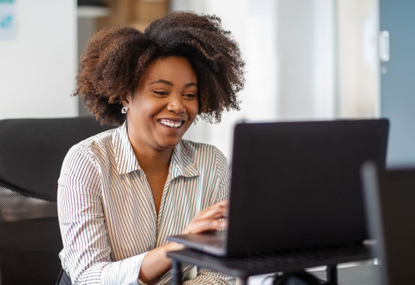 A professional black woman sits at her laptop in an office setting.