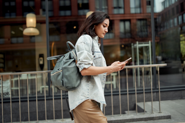 A woman in a jean jacket walks down the street viewing her phone.