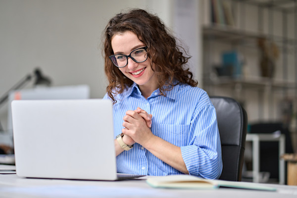 A woman in a collared shirt clasps her hands in front of her computer. 