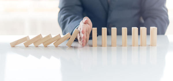 A white male hand stops wooden dominoes from falling on dominoes that are still standing