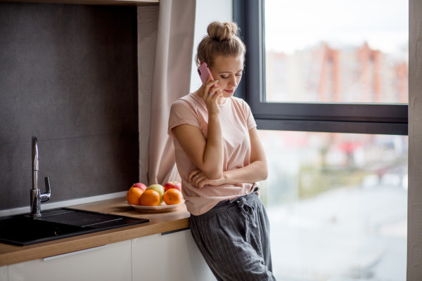 Young woman with bun talking on the phone while leaning on kitchen counter