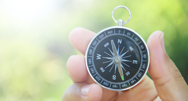 A hand holds a compass against a green background