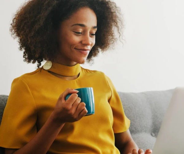 Woman in yellow shirt with coffee mug smiling.  JPG