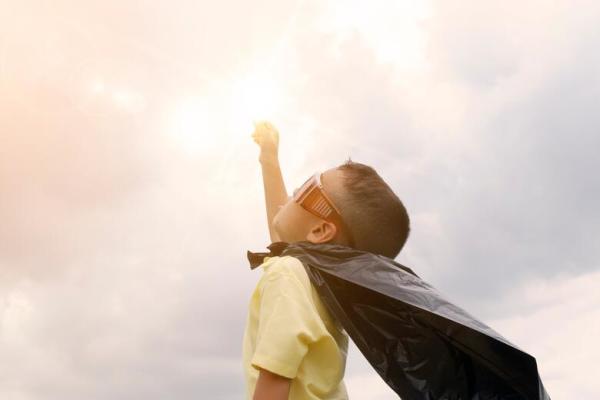 A child pretending to fly wearing a cape and sunglasses.  Hero.