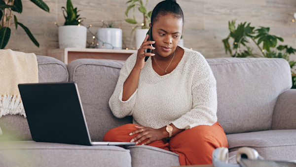 An African-American woman takes a phone call on her couch while in front of the computer