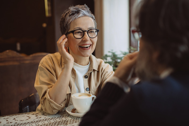 Grey-haired woman with glasses talking to a friend