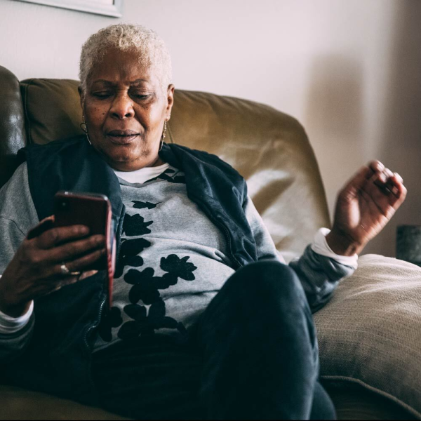 An older, white-haired black woman sits on a leather chair using her phone