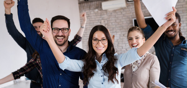 five people stand in a room with their arms in the air smiling far broader than necessary