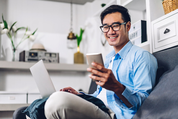 A smiling man sits on a couch looking at the phone in his hand