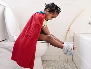Child with cape in bathroom on toilet
