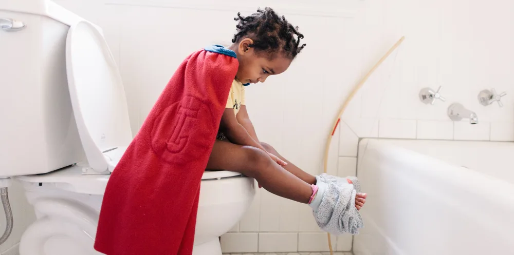Child with cape in bathroom on toilet