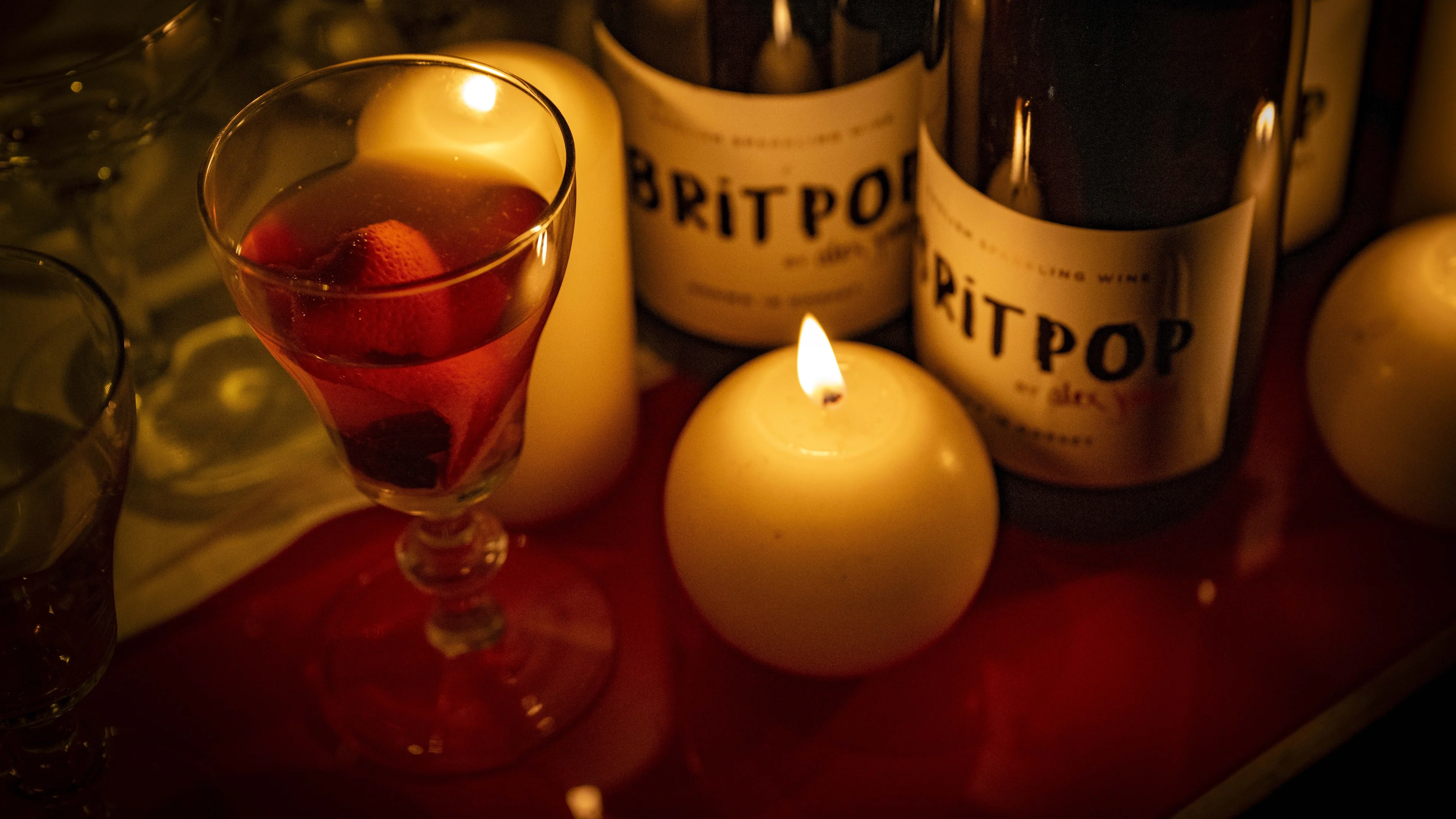 Glass of mulled drink beside bottles of sparkling wine and lit candles on a softly lit tasting table.