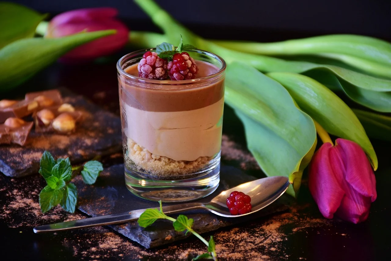 Layered chocolate mousse in a glass topped with raspberries and mint, with tulips and caramel pieces nearby.