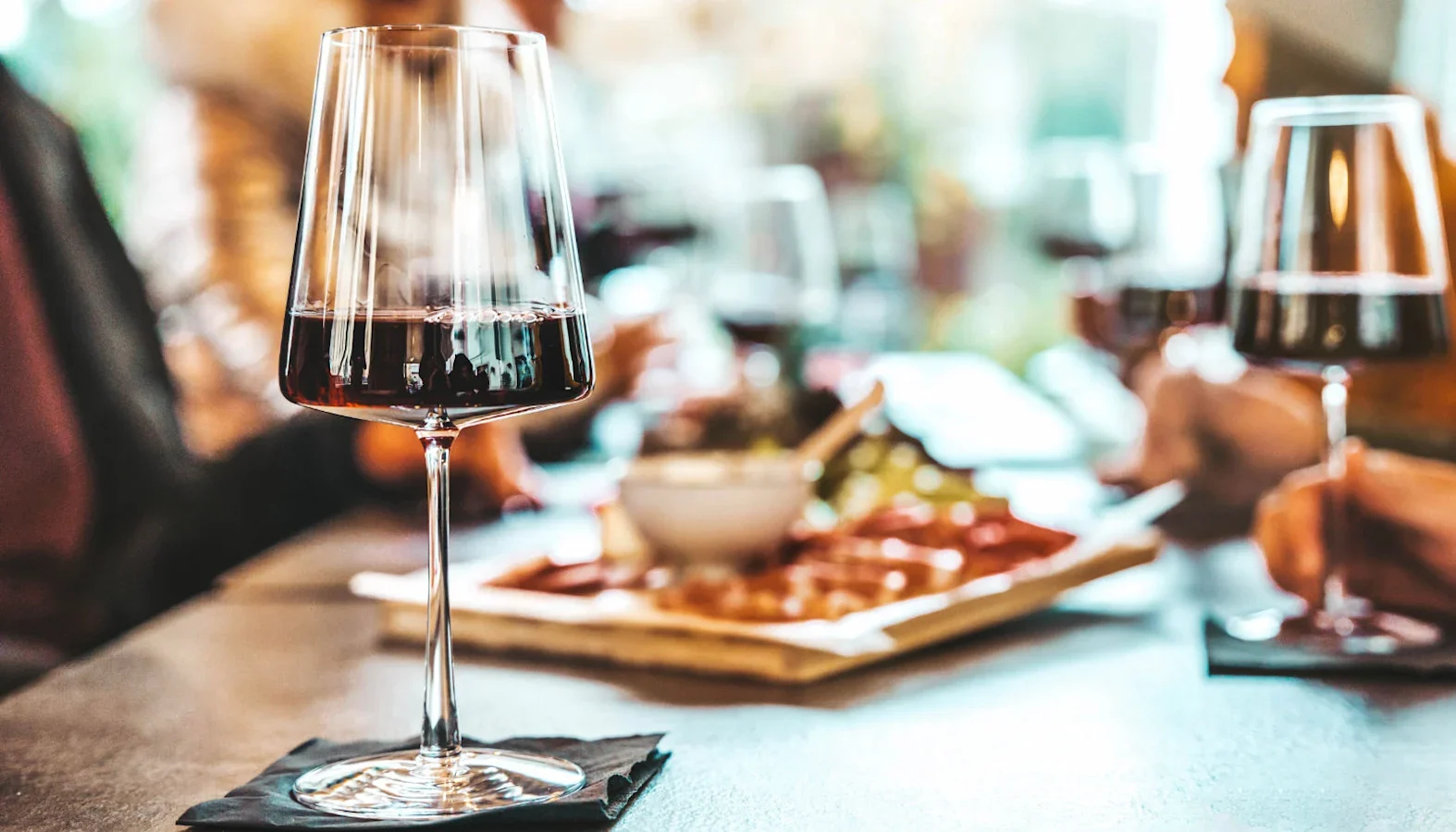 Glass of red wine on a table with food platters in the background at a social gathering.