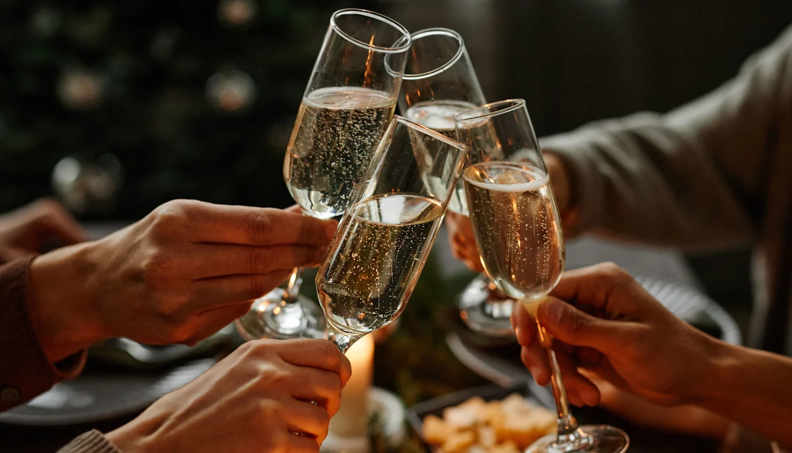 Group raising sparkling wine glasses for a toast at a candlelit gathering.
