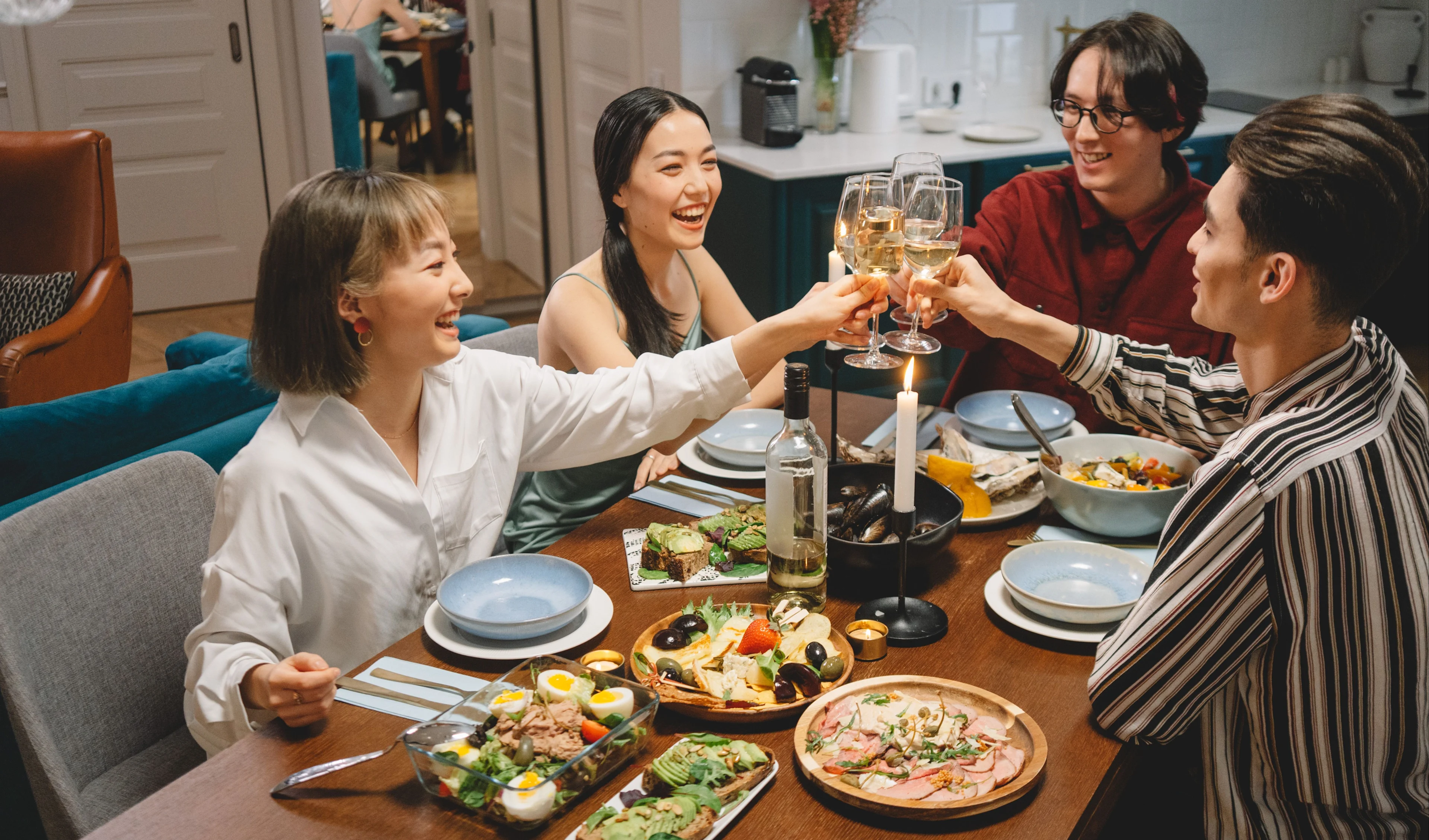 People raising glasses of white wine around a dining table filled with shared dishes and candles.