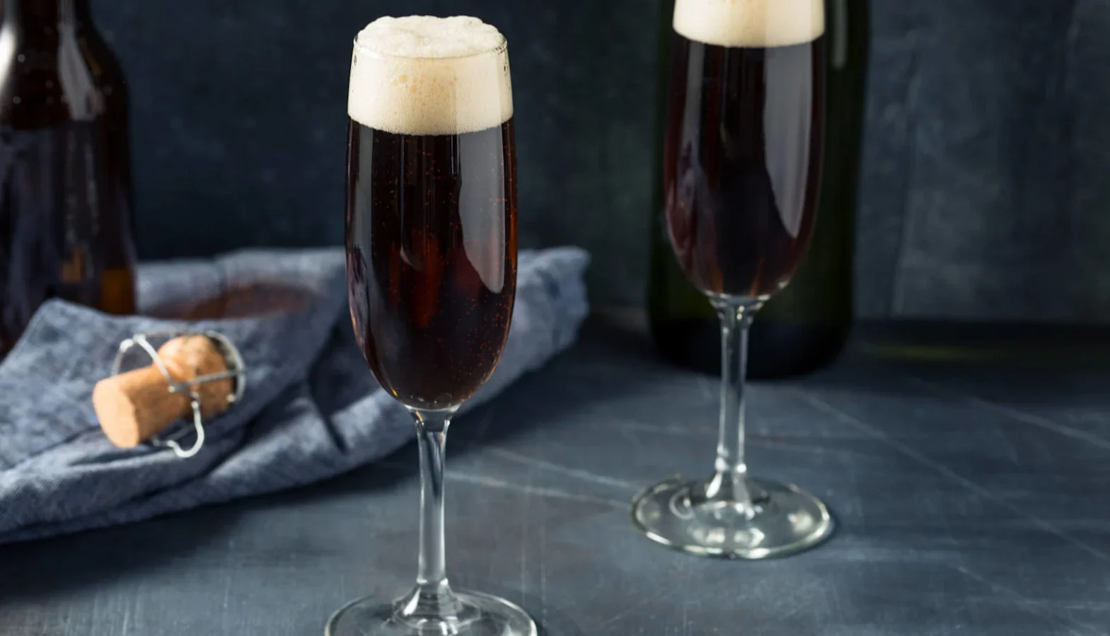 Two champagne flutes filled with dark beer and sparkling wine topped with foam.