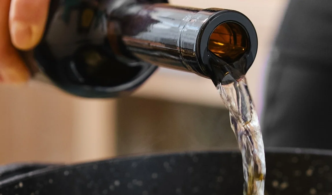 Wine being poured from a bottle into a cooking pot.