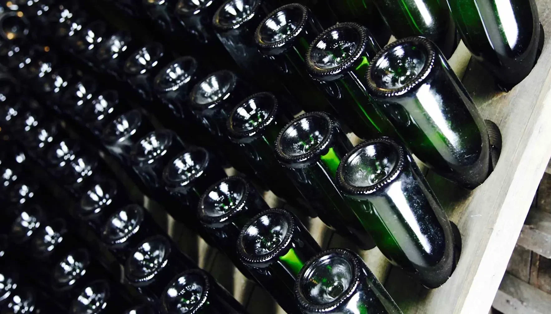Rows of sparkling wine bottles stored upside down in a riddling rack during production.