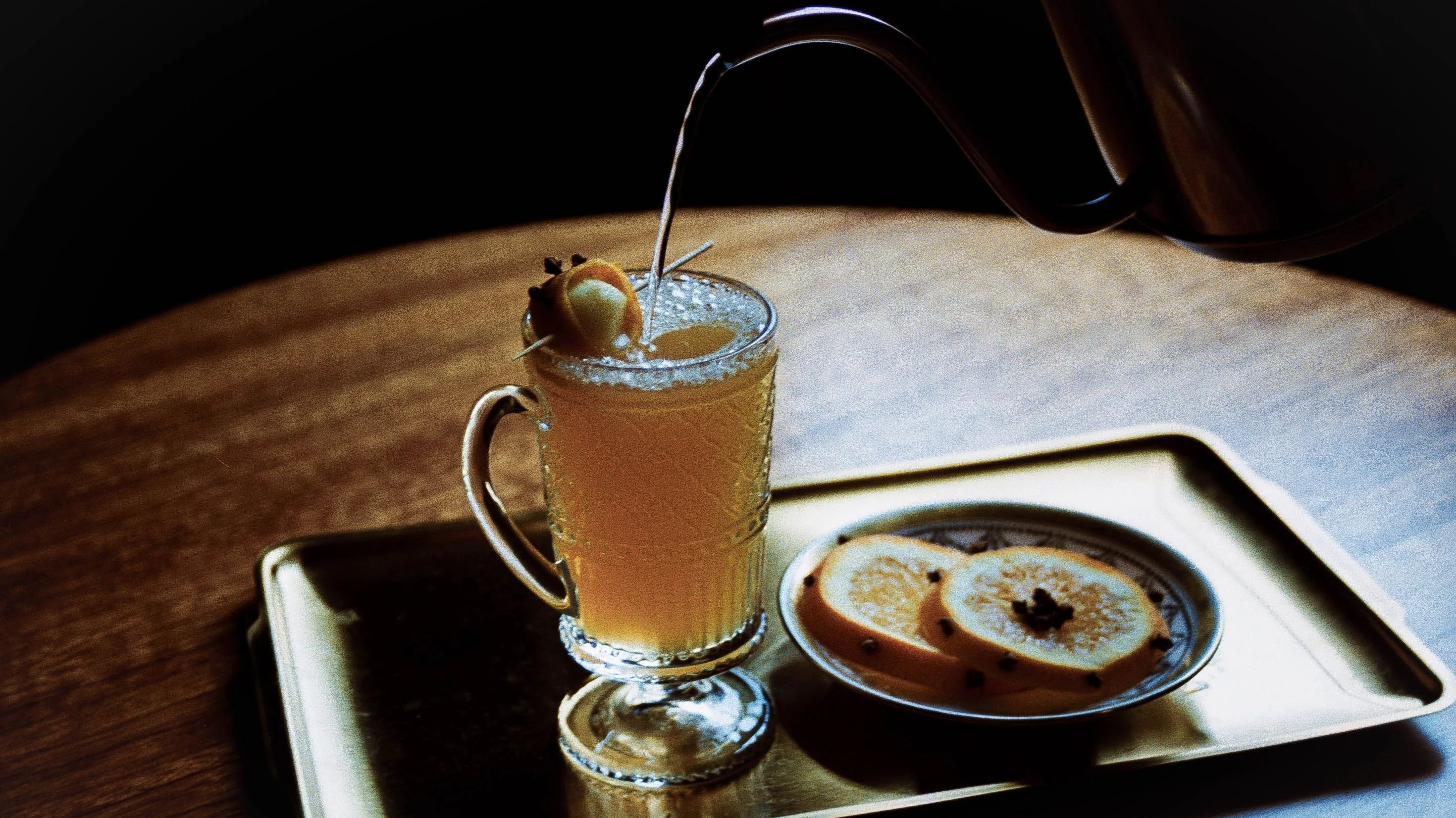 Hot whiskey cocktail being poured into a glass mug, served with apple slices.