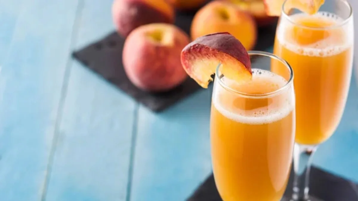Two peach Bellini cocktails in tall glasses, garnished with peach slices.