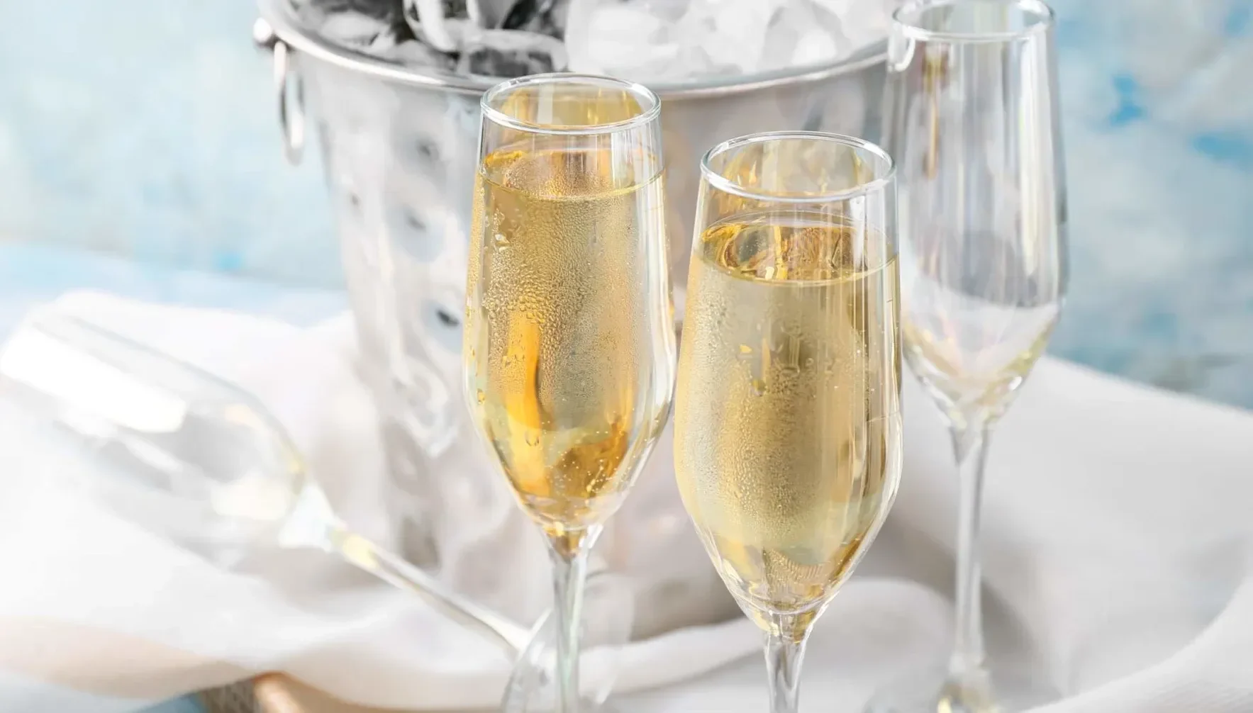 Two flutes of sparkling wine beside an ice bucket, with condensation visible on the glasses.
