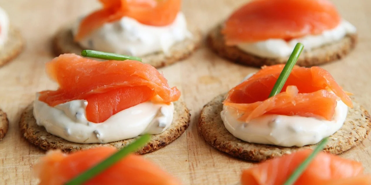 Small crackers topped with creamy spread and slices of smoked salmon with chives.