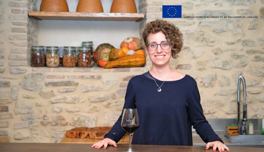 A person standing at a counter with a glass of red wine in a rustic kitchen setting.