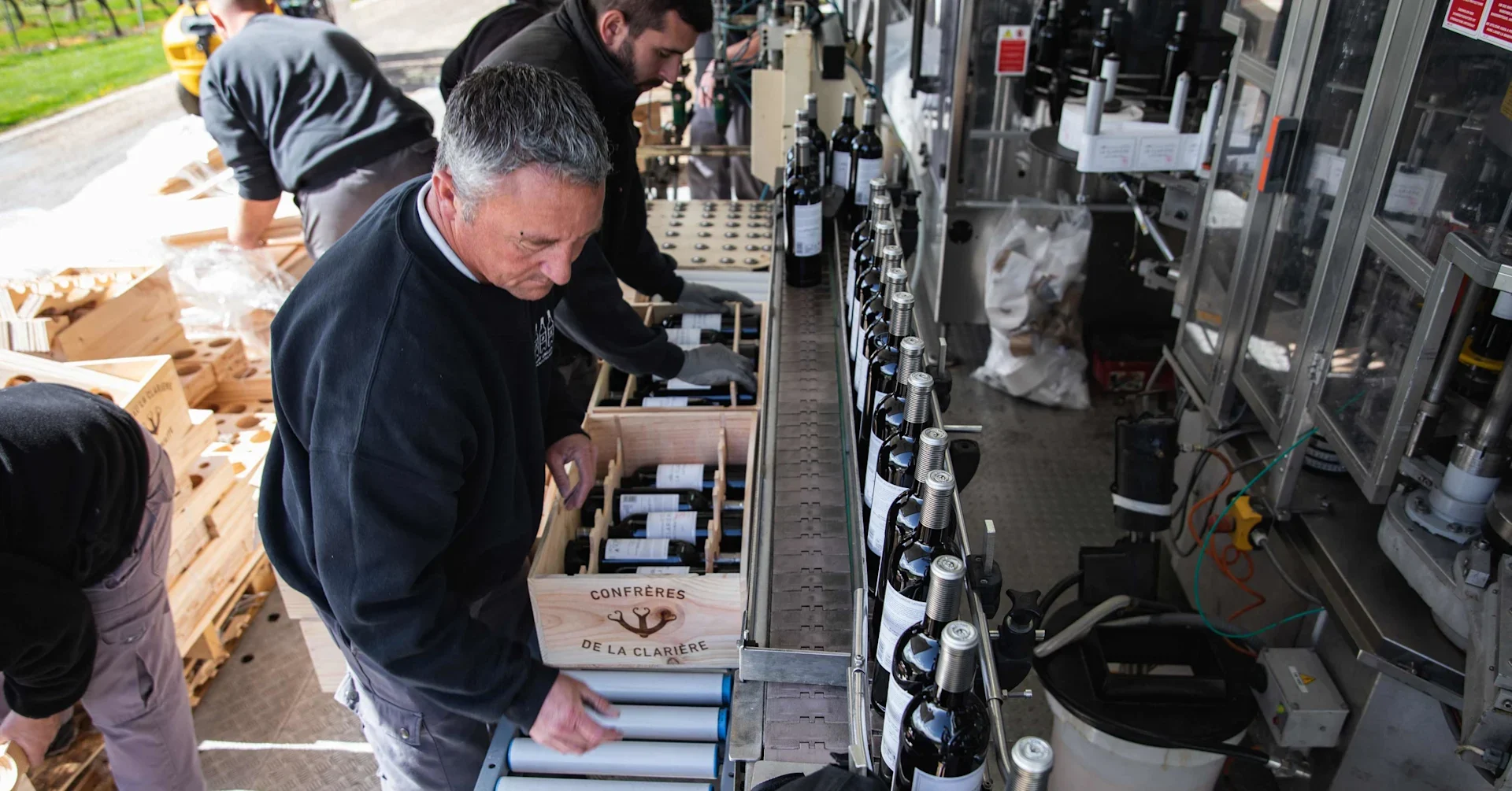 People standing in a bottling line packing freshly bottled wine into wooden cases.