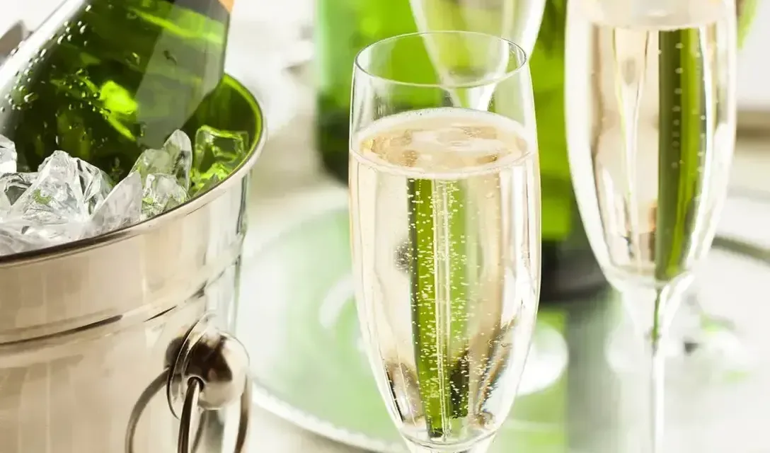 Champagne bottle in an ice bucket beside a glass of sparkling wine on a bright green and silver background.