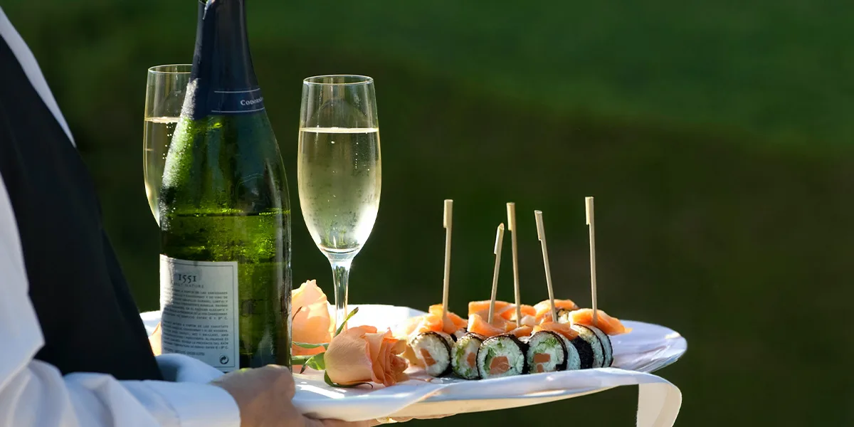 Tray with sushi rolls and salmon bites served alongside a bottle and glasses of sparkling wine.