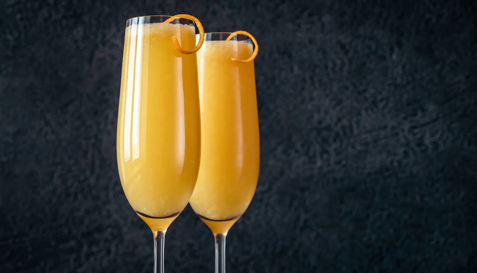 Two champagne flutes with orange cocktail garnished with orange peel twists.