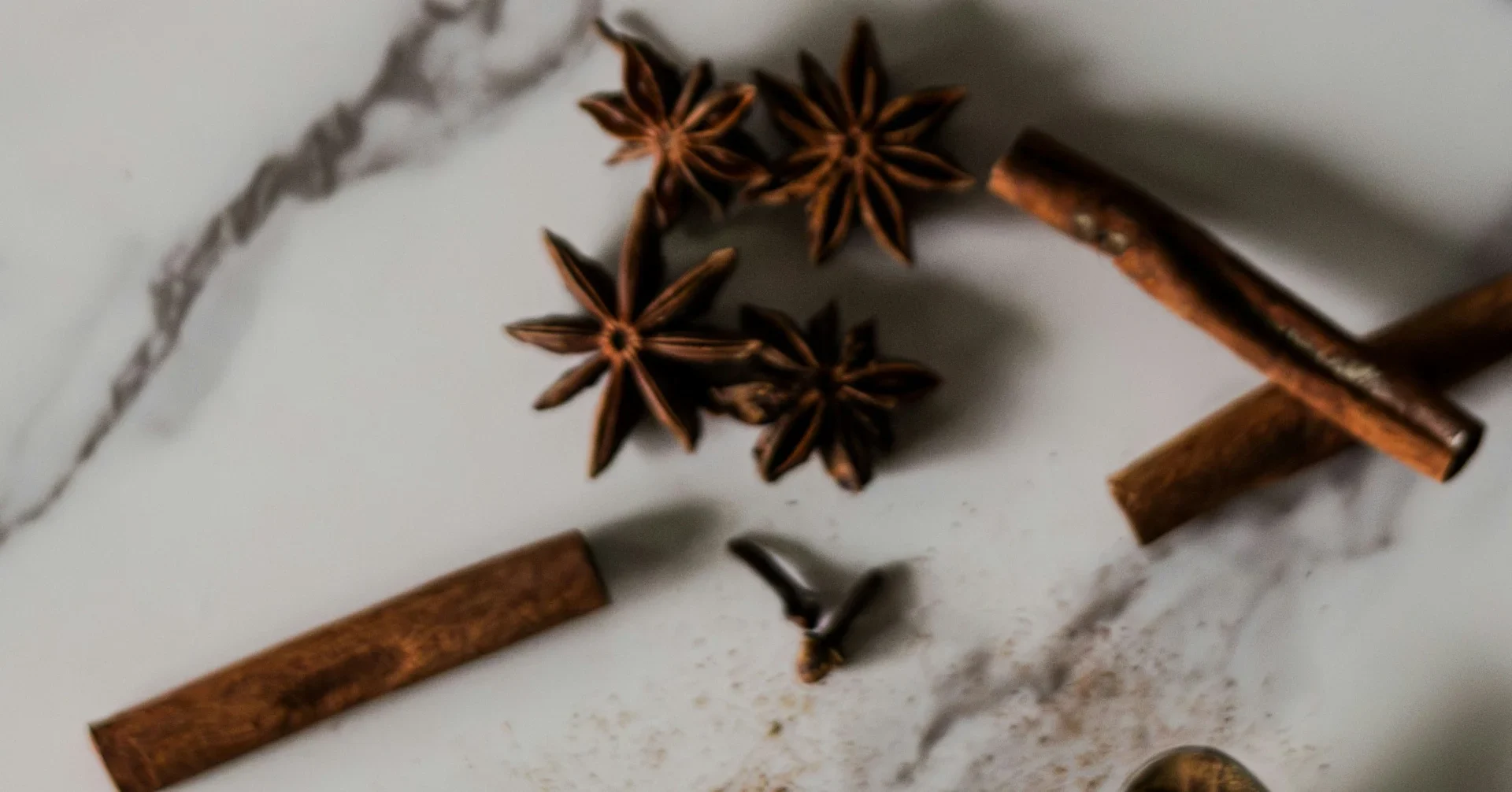 Star anise pods, cinnamon sticks, and a clove arranged on a white marble surface.