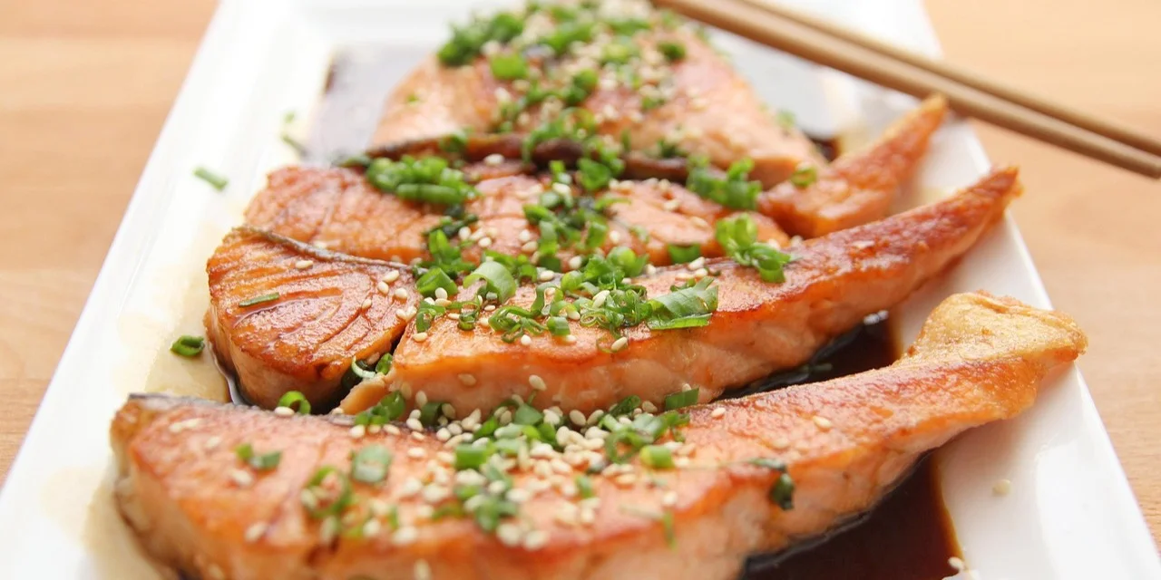 Cooked salmon pieces in soy and teriyaki sauce topped with sesame seeds and chopped herbs