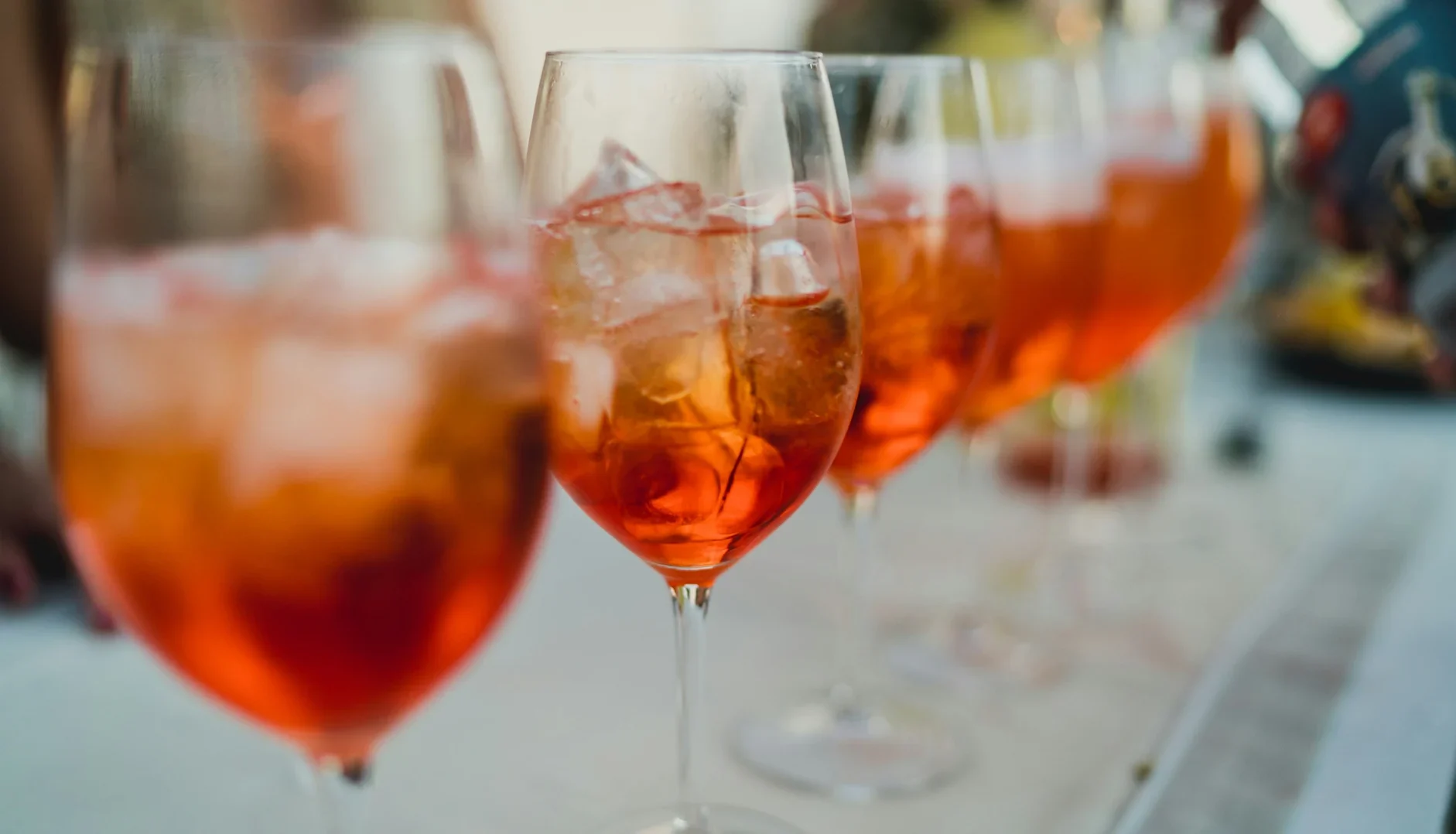 Row of Aperol spritz cocktails in stemmed glasses filled with ice.