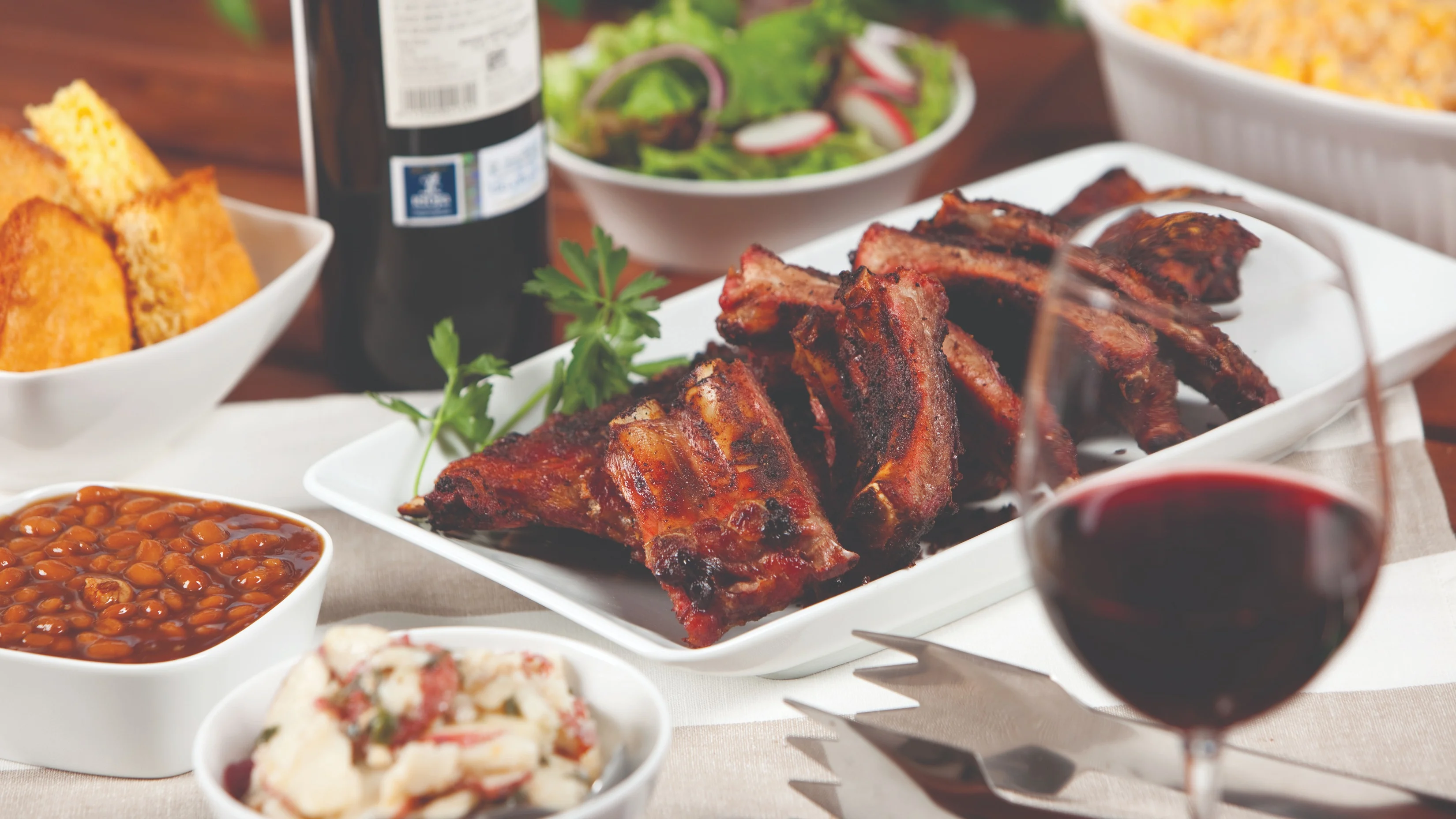 Plate of barbecued pork ribs served with baked beans, salad and a glass of red wine.