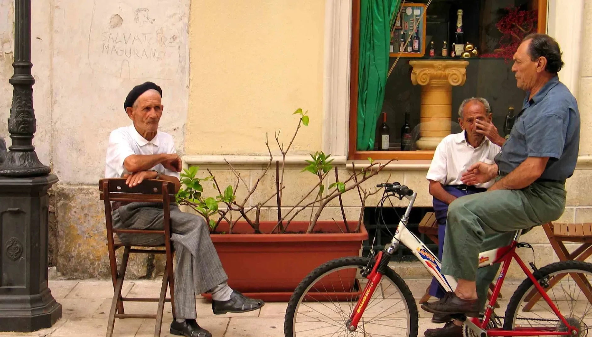 People sitting and chatting outside a café on a narrow street in a traditional town in Puglia.