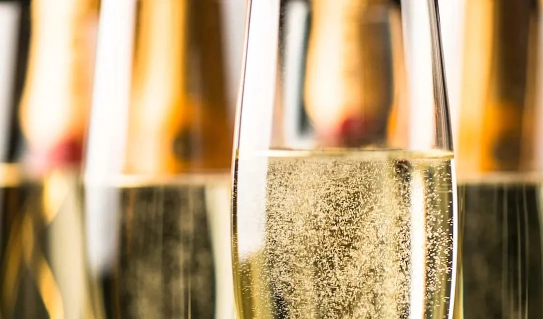 Close-up of several champagne flutes filled with sparkling wine, showing rising bubbles with blurred bottles in the background.